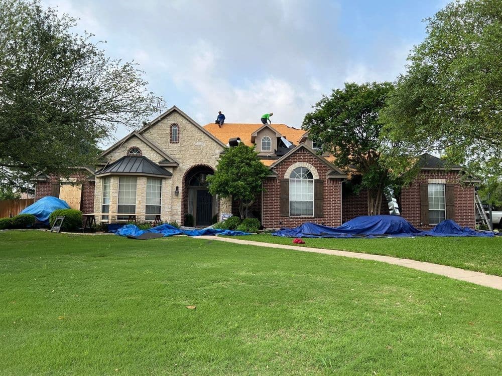 Roofing project in progress on a suburban home with tarps and workers on the roof.