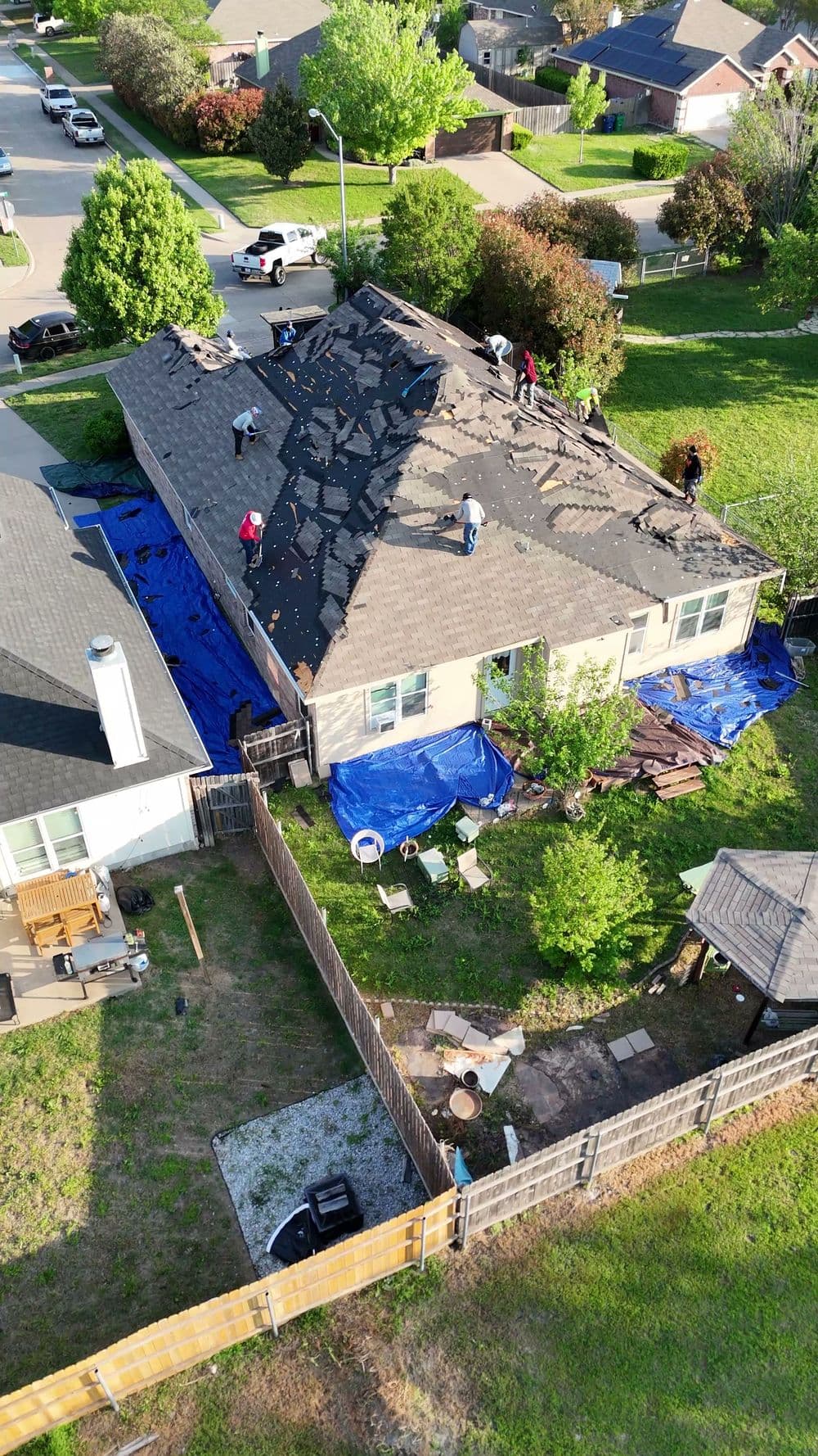 Roof replacement in progress with workers and protective tarps on a suburban home.