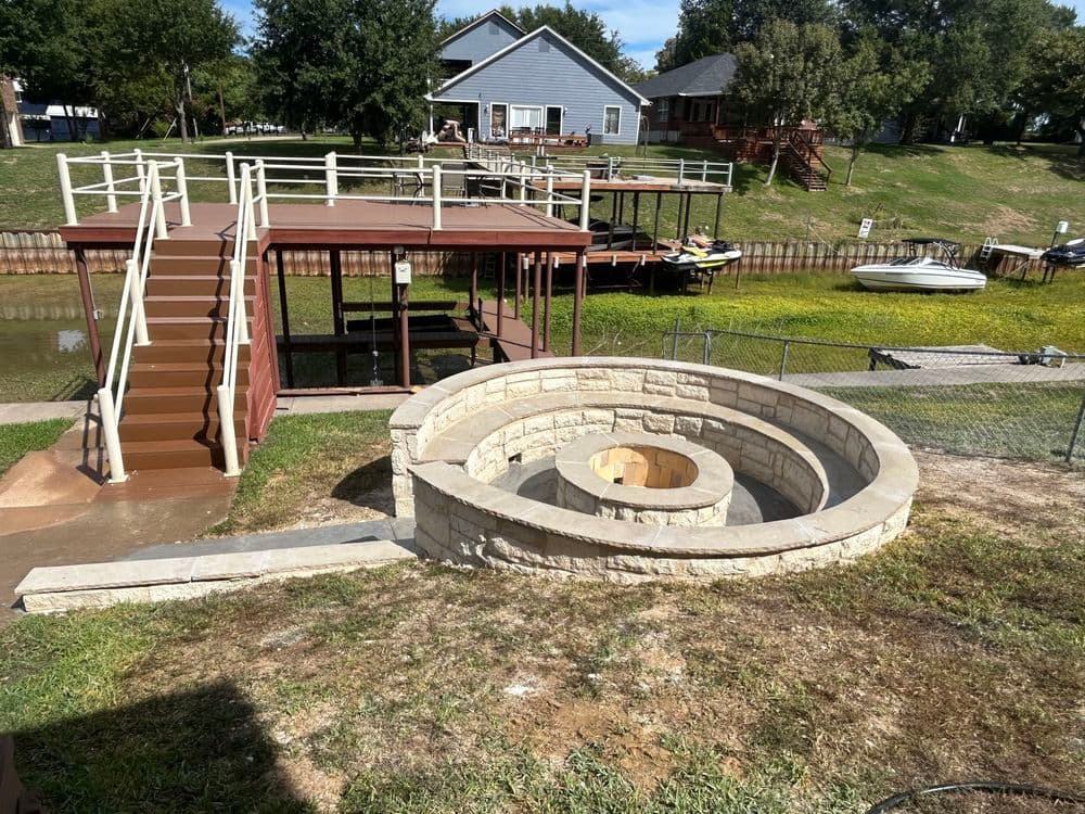 Spiral stone water feature next to dock and boats along a grassy lakeside property.