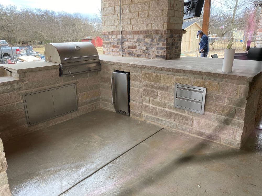 Outdoor kitchen featuring built-in grill, stone countertop, and storage cabinets. Modern design.